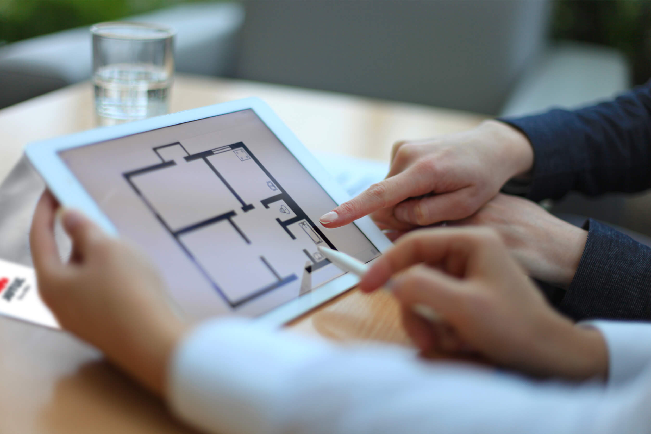 Hände, die auf ein iPad mit einem Blatt der Raumverteilung in einem Haus zeigen.